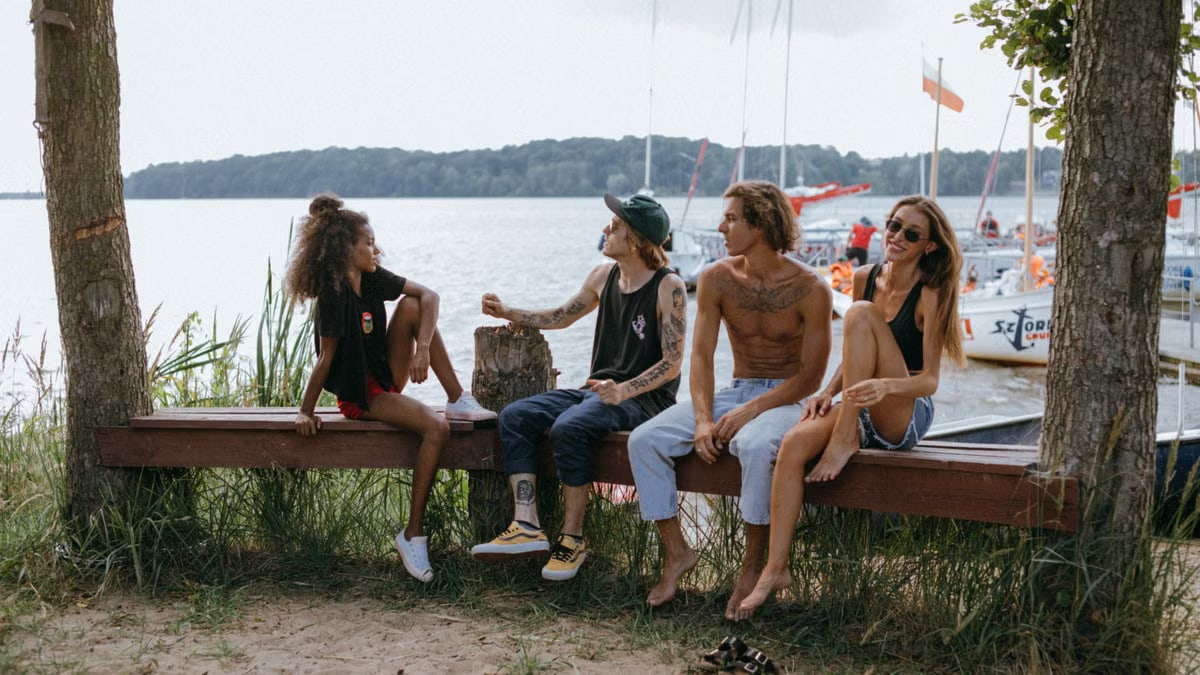 A diverse group of friends enjoying leisure time by a picturesque lakeside with boats in the background.